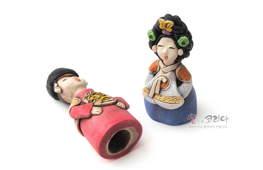 [텍스트: 샵오브코리아 대한민국의 품격까지 전합니다.] 황토를 빚어 구운 도자기 인형 한 쌍, 붉은색·청색 한복과 금색 용 문양, 꽃 장식 머리와 소박한 질감이 돋보이는 왕과 왕비 형상 전통 인형