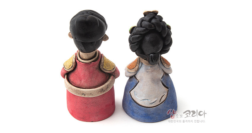 [텍스트: 샵오브코리아 대한민국의 품격까지 전합니다.] 붉은색·청색 한복 차림 황토 도자기 왕과 왕비 인형의 뒷모습, 입체 머리장식과 소맷단·견장 부분 채색 표현 특징인 전통 조형 인형