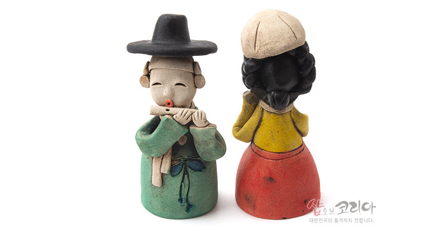 [텍스트: 샵오브코리아 대한민국의 품격까지 전합니다.] 황토 재질 수공 조각 선비와 여인 인형 한 쌍, 녹색 도포와 노랑 저고리·붉은 치마의 대비, 검정 갓과 흰 두건으로 표현한 한국 전통 복식 장식 인형