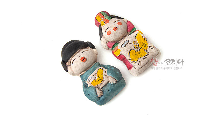 [텍스트: 샵오브코리아 대한민국의 품격까지 전합니다.] 황토 느낌 도자 재질의 신랑신부 자석 인형, 청록·홍색 한복과 노란 봉황 문양, 손도장 질감이 살아 있는 전통 미니어처 소품