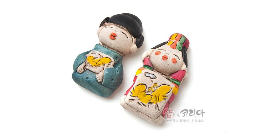 [텍스트: 샵오브코리아 대한민국의 품격까지 전합니다.] 황토 느낌 도자 재질 신랑신부 인형 자석, 청록·홍색 한복과 노란 나비·새 문양의 수채화풍 채색이 돋보이는 전통 소품