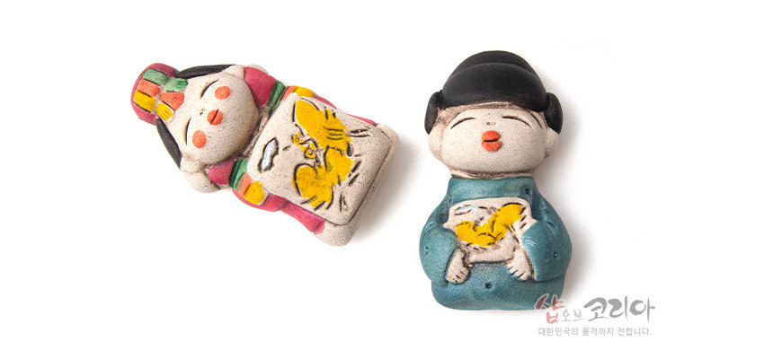 [텍스트: 샵오브코리아 대한민국의 품격까지 전합니다.] 황토 느낌 도자 재질의 신랑신부 모양 냉장고 자석, 청록색·홍색 한복과 노란 나비 문양 채색이 돋보이는 인테리어 소품