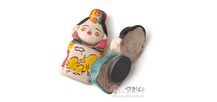 [텍스트: 샵오브코리아 대한민국의 품격까지 전합니다.] 황토 느낌 도자 재질의 신랑신부 자석, 청록·홍색 한복과 노란 새 문양, 후면 원형 자석 부착 인형형 소품 이미지 설명