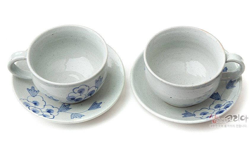 [텍스트: 샵오브코리아 대한민국의 품격까지 전합니다.] 회백색 분청사기 재질의 커피잔과 받침 세트, 수묵화풍 청색 목단 꽃문양과 자연스러운 유약 번짐이 어우러진 2인용 구성