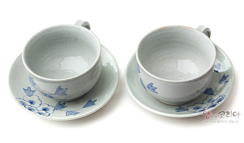 [텍스트: 샵오브코리아 대한민국의 품격까지 전합니다.] 회백색 분청 도자 재질에 청색 목단 꽃문양이 수묵화풍으로 장식된 2인용 커피잔과 받침 세트 모습