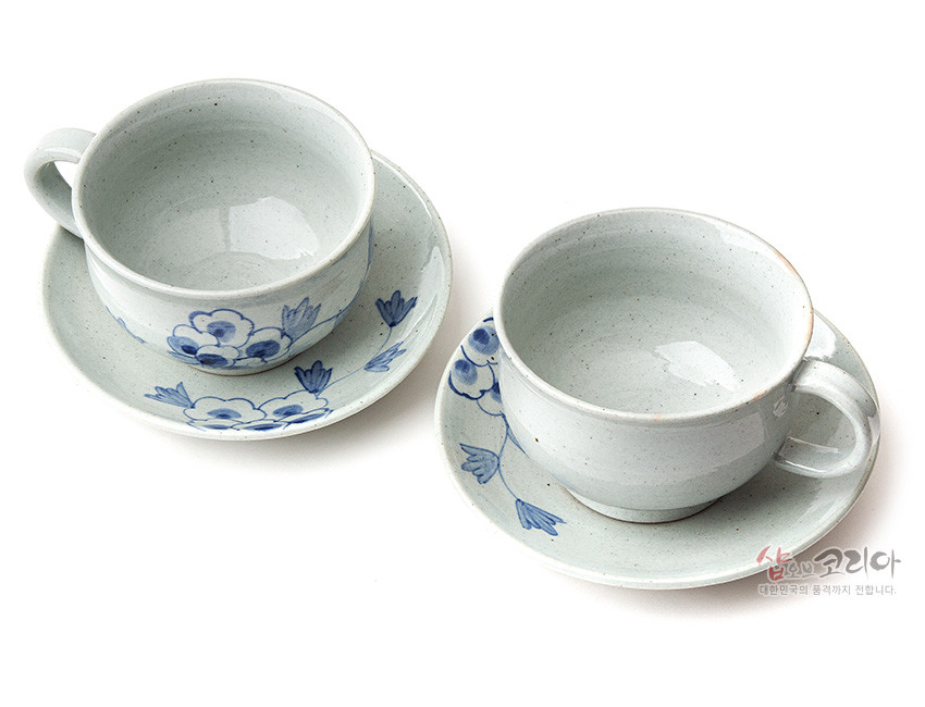 [텍스트: 샵오브코리아 대한민국의 품격까지 전합니다.] 청회색 분청 도자 재질, 수묵화풍 청색 목단 꽃문양이 둘린 2인용 커피잔과 받침 세트 모습