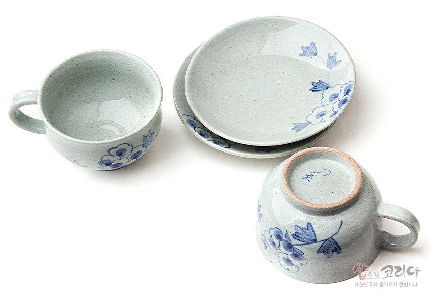[텍스트: 샵오브코리아 대한민국의 품격까지 전합니다.] 담백한 분청사기 재질에 회백색 유약을 입히고, 청색 수묵화풍 목단과 잎사귀 문양을 핸드페인팅한 커피잔과 받침 접시 2인 세트 구성