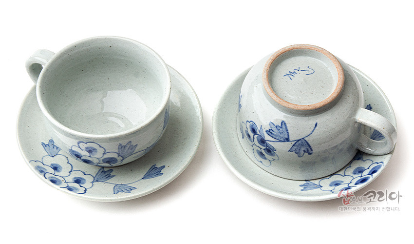 [텍스트: 샵오브코리아 대한민국의 품격까지 전합니다.] 회백색 분청 도자기 재질에 청색 목단 꽃문양이 수묵화풍으로 그려진 커피잔과 받침 2인 세트 구성
