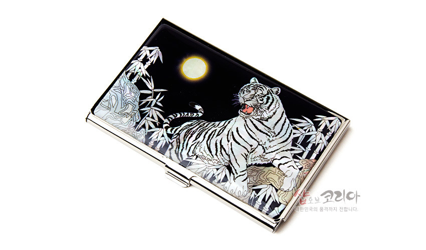 [텍스트: 샵오브코리아 대한민국의 품격까지 전합니다.] 자개 상감 기법으로 백호와 대나무, 만월 문양을 표현한 금속 명함케이스, 흑색 바탕의 광택 있는 표면 구성
