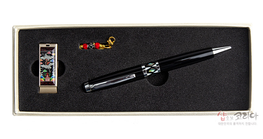 [텍스트: 샵오브코리아 대한민국의 품격까지 전합니다.] 흑색 옻칠 볼펜과 금속 USB에 자개 상감 흉배 학·구름 문양을 넣고, 붉은색·초록색 비단 매듭 장식을 더한 세트 모습