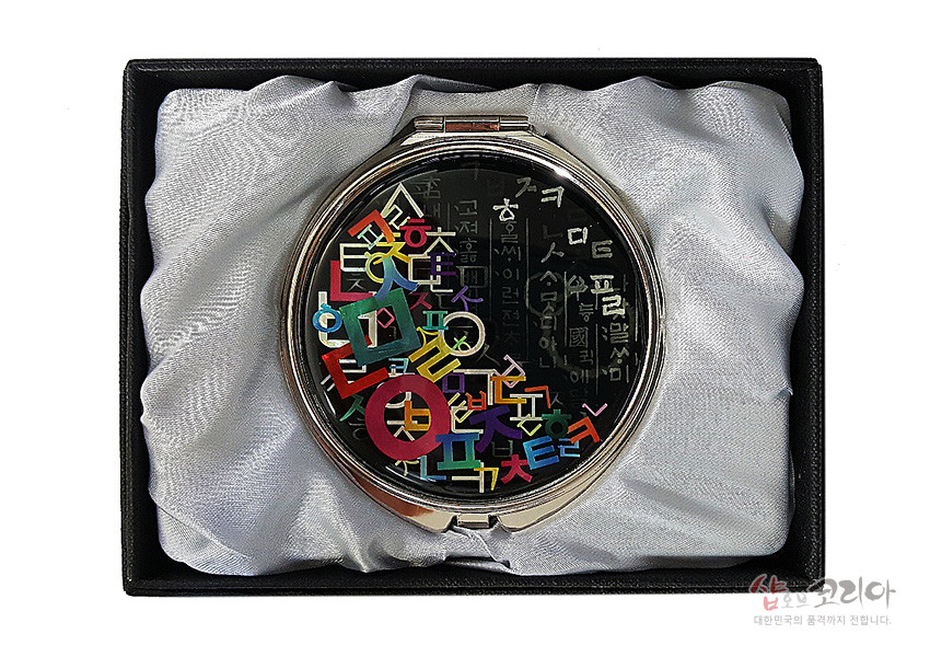 [텍스트: 일부 한글 자음과 문장] 검은 옻칠 바탕 위 자개 느낌의 다채로운 한글 자음 문양이 상감된 금속 테두리 원형 손거울 디자인