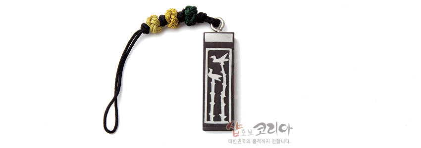 [텍스트: 샵오브코리아 대한민국의 품격까지 전합니다.] 흑단 직사각 펜던트에 흰색 상감 솟대와 새 문양 장식, 검정 끈에 노랑·연두 전통 매듭 포인트 열쇠고리 디자인