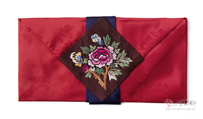 [텍스트: 샵오브코리아 대한민국의 품격까지 전합니다.] 붉은 비단에 은은한 꽃잎 문양을 넣고, 중앙에 모란과 나비 자수를 놓은 감색 끈 장식의 봉투형 예단보 디자인