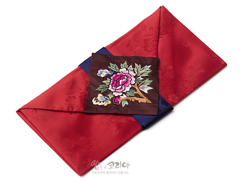 [텍스트: 샵오브코리아 대한민국의 품격까지 전합니다.] 붉은 비단에 은은한 꽃문양을 짜넣고, 중앙에 목단·나비 자수를 놓은 갈색 비단 패널과 남색 비단 장식을 더한 봉투형 예단보 디자인
