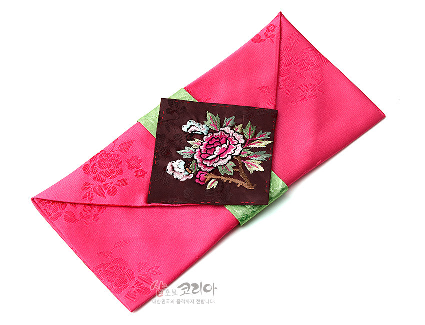 [텍스트: 샵오브코리아 대한민국의 품격까지 전합니다.] 분홍 비단 바탕에 은은한 꽃무늬 짜임, 연두색 비단 띠와 짙은 고동색 바탕의 화려한 목단 자수 장식이 어우러진 봉투형 예단보 이미지 설명