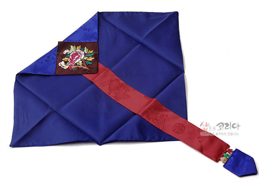 [텍스트: 샵오브코리아 대한민국의 품격까지 전합니다.] 짙은 청색 비단 바탕에 장수를 상징하는 은은한 문양, 붉은 비단 띠와 모란 자수 장식이 어우러진 봉투형 예단보 디자인