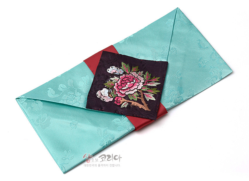 [텍스트: 샵오브코리아 대한민국의 품격까지 전합니다.] 청록 비단에 꽃문 양각 직조하고 붉은 비단 띠 위 검정 바탕 목단·나비 자수 장식한 봉투형 예단보 디자인