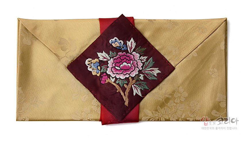 [텍스트: 샵오브코리아 대한민국의 품격까지 전합니다.] 황금색 꽃문양 비단에 붉은 비단 띠와 목단·나비 자수가 놓인 사각 장식이 더해진 봉투형 예단보 디자인
