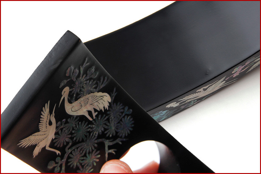 무광 흑색 옻칠 바탕 위에 자개 상감 기법으로 송학과 꽃 문양을 정교하게 장식한 곡선형 나전칠기 와인홀더 부분 클로즈업 이미지 설명