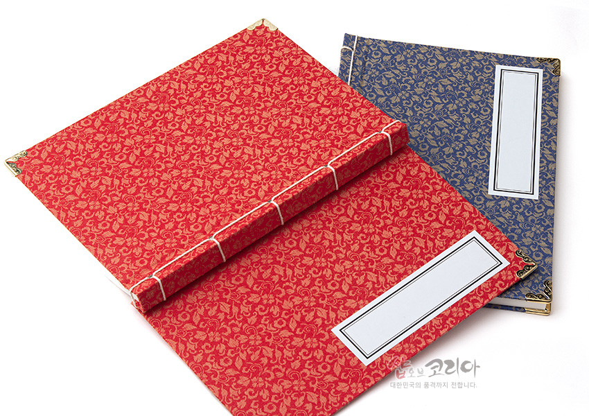 [텍스트: 샵오브코리아 대한민국의 품격까지 전달합니다.] 붉은 비단에 금색 전통 문양을 직조한 표지와 금속 모서리 장식, 흰 실로 묶은 오침 제본이 특징인 전통 노트 모습