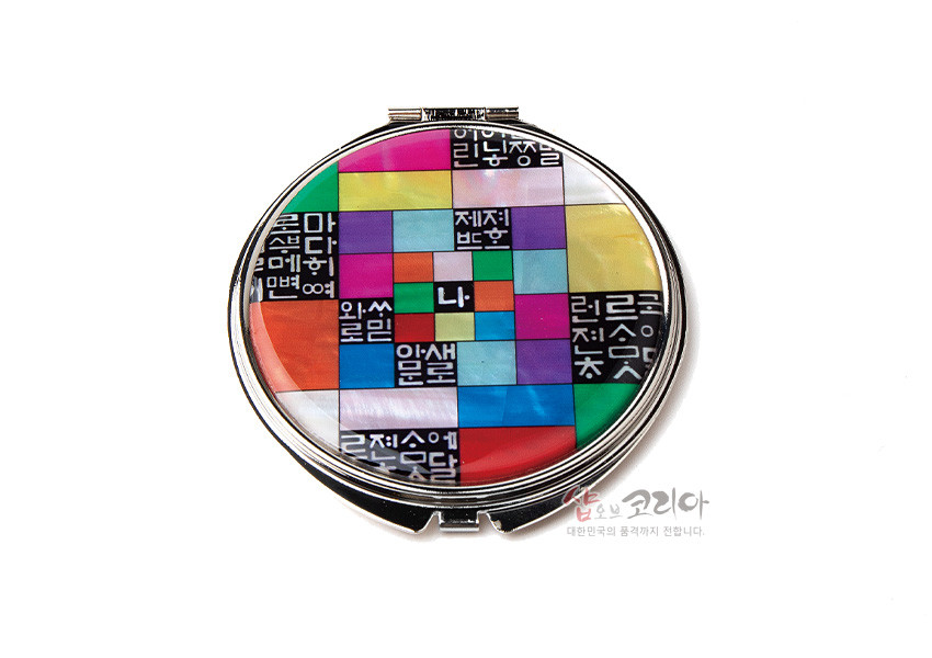 [텍스트: 나] 자개 상감과 옻칠 기법의 금속 손거울, 오방색 조각보 배경과 흑백 훈민정음 자모 문양이 어우러진 원형 디자인