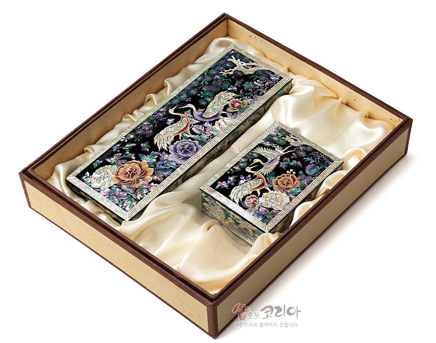 [텍스트: 샵오브코리아 대한민국의 혼과 정까지 전합니다.] 흑색 옻칠 바탕 위 자개 상감으로 송학과 모란, 소나무, 구름 문양을 오방색 계열로 수놓은 필함·명함함 세트 모습