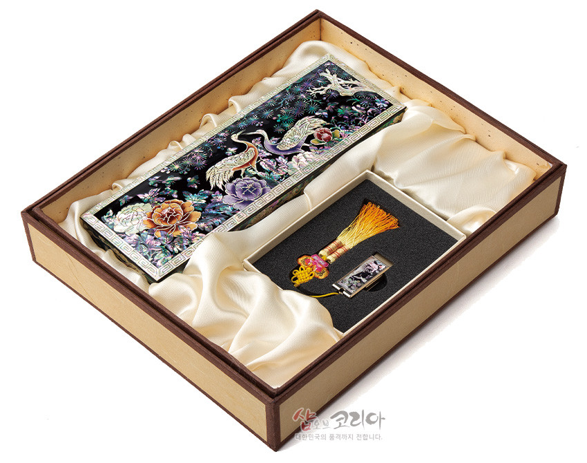 [텍스트: 샵오브코리아 대한민국의 품격까지 전합니다.] 흑색 옻칠 바탕에 자개 상감으로 송학·모란·소나무 문양을 넣은 직사각 필함과 노랑 술 매듭 장식 자개 USB가 실크 느낌 내피에 담긴 세트 구성