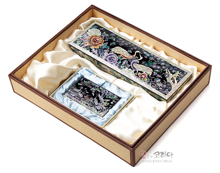 [텍스트: 샵오브코리아 대한민국의 품격까지 전합니다.] 흑색 옻칠 위 자개 상감 기법, 송학·모란·소나무 문양이 다채로운 색감으로 표현된 필함과 명함케이스 세트 이미지 설명