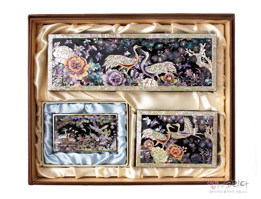 [텍스트: 샵오브코리아 대한민국의 품격까지 전합니다.] 흑색 옻칠 바탕 위 자개 상감 기법으로 송학과 소나무, 모란을 다채로운 오방색 톤으로 표현한 필함·명함함·명함케이스 세트 구성