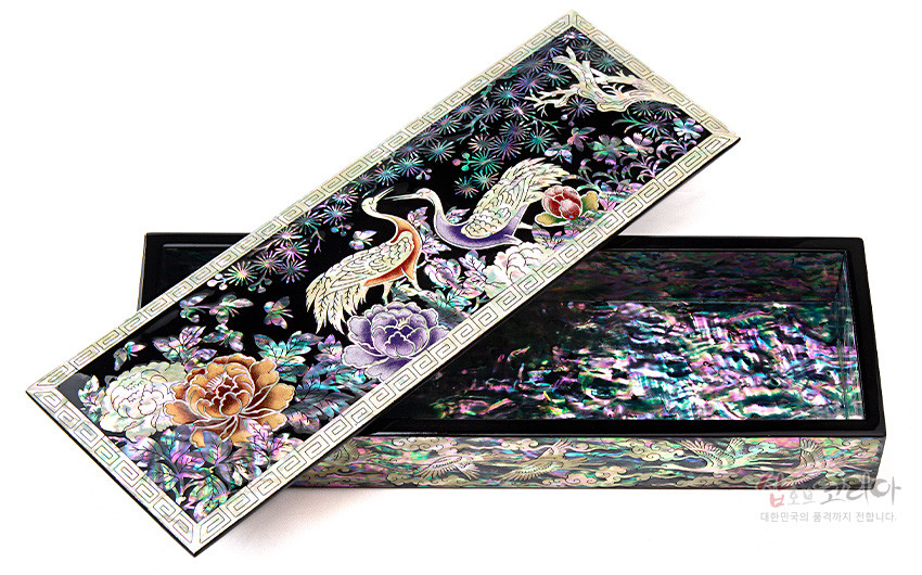 [텍스트: 샵오브코리아 대한민국의 품격까지 전합니다.] 흑색 옻칠 바탕 위 자개 상감 기법으로 송학과 모란, 소나무 문양을 섬세하게 표현한 직사각 필함 디자인