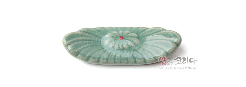 [텍스트: 샵오브코리아 대한민국의 품격까지 전합니다.] 옅은 비취색 유약을 입힌 청자 수저받침, 음각 꽃무늬와 중앙의 붉은 점 포인트 장식
