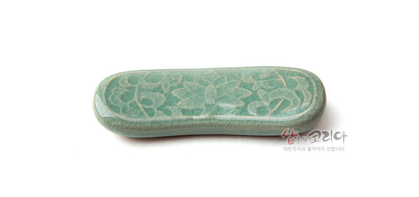 [텍스트: 샵오브코리아 대한민국의 품격까지 전합니다.] 비취색 청자 재질에 유려한 곡선형으로 제작된 수저받침, 표면에 음각 당초무늬를 정교하게 새겨 넣은 디자인
