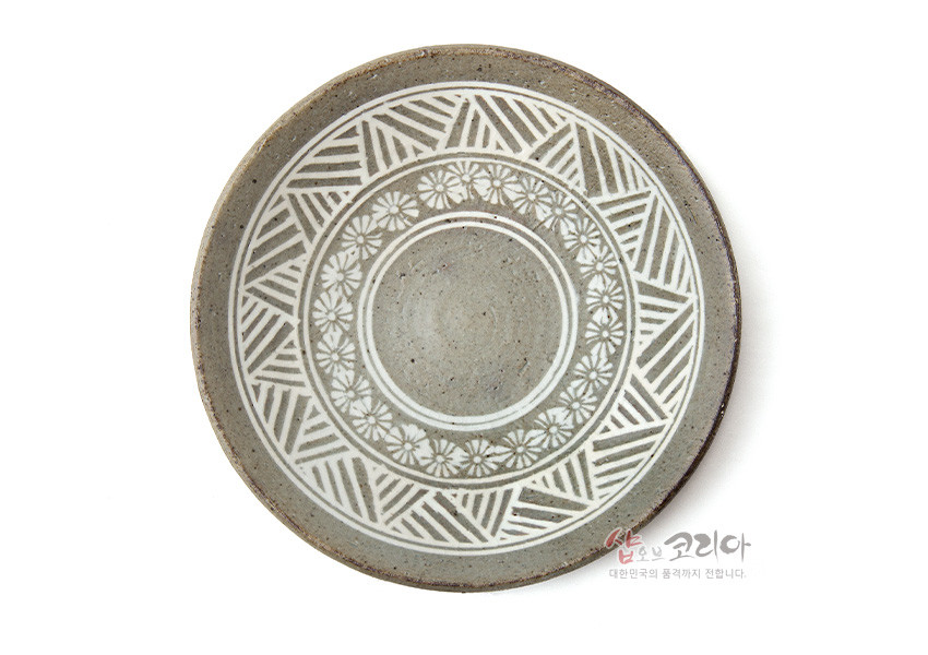[텍스트: 샵오브코리아 대한민국의 품격까지 전합니다.] 분청사기 재질, 백색 상감 기법으로 국화문과 기하학 문양을 둘러 장식한 원형 받침 접시 모습