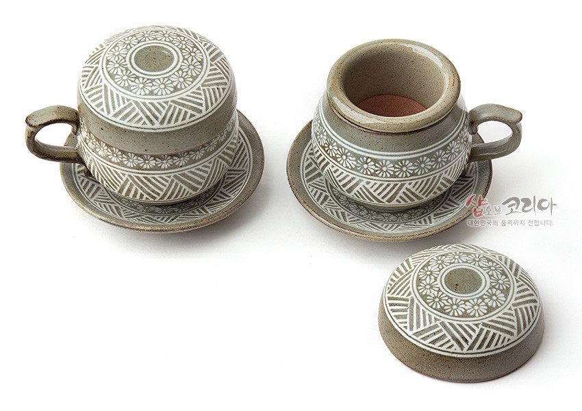 [텍스트: 샵오브코리아 대한민국의 품격까지 전합니다.] 분청사기에 백색 상감 기법으로 국화문과 기하학 문양을 두른 회갈색 2인용 뚜껑 다기잔과 받침 세트 구성