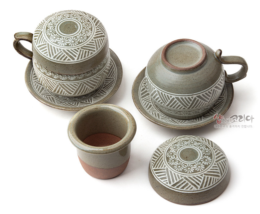 [텍스트: 샵오브코리아 대한민국의 품격까지 전합니다.] 분청사기 재질에 백색 상감 기법으로 국화문과 기하학 문양을 둘러 장식한 뚜껑잔과 받침 포함 2인 다기잔 세트 모습