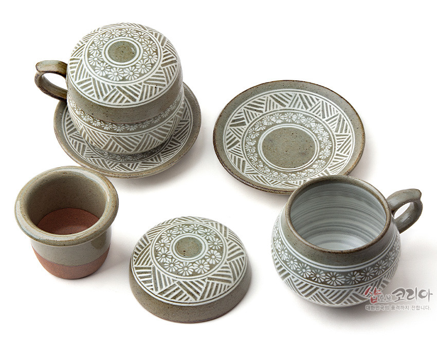 [텍스트: 샵오브코리아 대한민국의 품격까지 전합니다.] 분청사기 재질에 백색 상감 기법으로 국화문과 기하학 문양을 둘러 새긴 2인용 다기잔과 받침 접시, 거름망 구성의 세트 모습