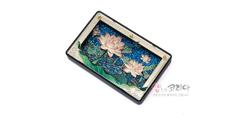 [텍스트: 샵오브코리아 대한민국의 품격까지 전합니다.] 청색 수면 배경 위 금속 양각 기법으로 표현한 연꽃과 연잎, 가장자리에 은색·금색 장식 문양을 두른 직사각형 입체 마그넷 디자인