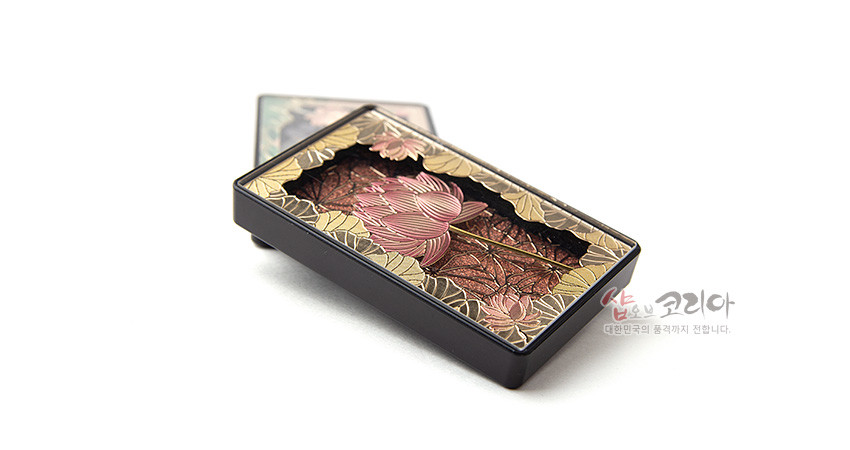 [텍스트: 샵오브코리아 대한민국의 품격까지 전합니다.] 금속 재질 바탕 위 핑크색 연꽃과 황금빛 연잎을 양각 기법으로 표현한 직사각형 마그넷, 갈색 배경과 검정 테두리의 대비가 돋보이는 전통 문양 장식