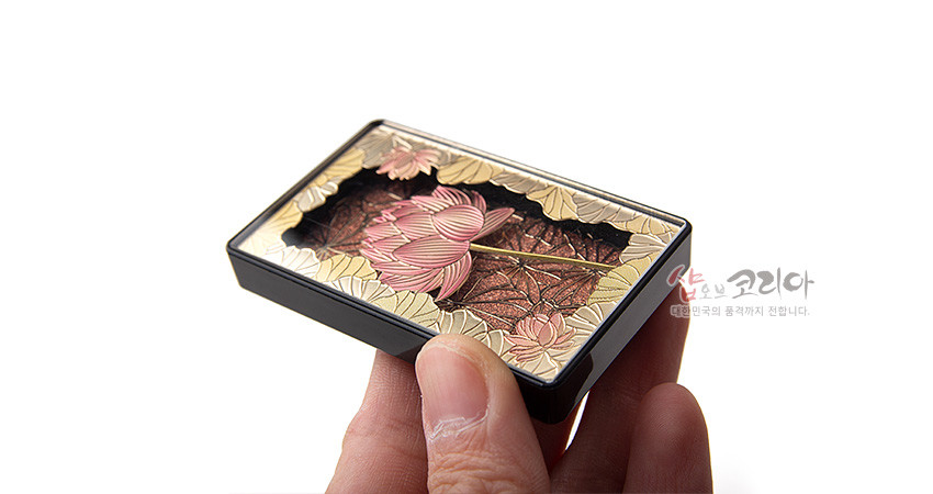[텍스트: 샵오브코리아 대한민국의 품격까지 전합니다.] 금속 재질 바탕에 양각 기법으로 표현된 분홍 연꽃과 황금빛 연잎 문양, 적갈색 배경과 흑색 테두리가 조화를 이루는 직사각형 입체 마그넷 모습