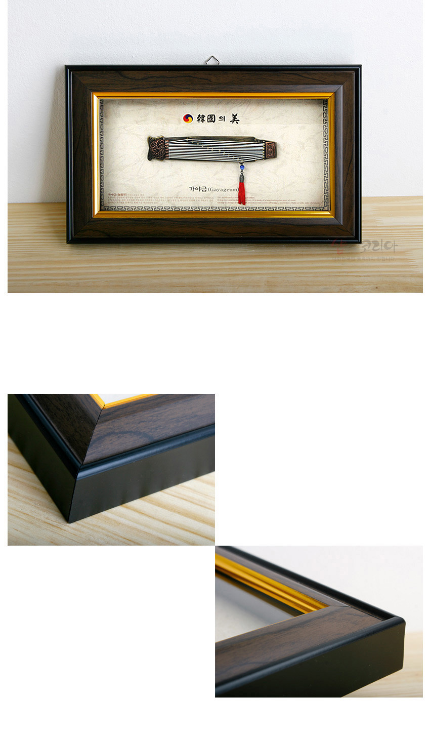 [텍스트: 韓國의 美 / 가야금(Gayageum)] 짙은 우드톤과 흑색 테두리 액자 속 금속 가야금 모형, 청색 구슬과 홍색 술 장식이 어우러진 전통 악기 장식 이미지