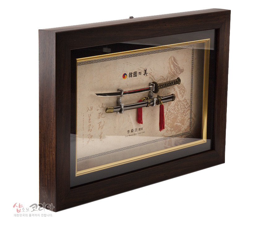 [텍스트: 韓國의美, 李舜臣 將軍, Shop of Korea 대한민국의 품격까지 전합니다.] 짙은 목재 액자 속 금속 이순신 장검과 칼집, 황금 문양 장식과 붉은 술, 전통 문양 배경지의 조화로운 구성