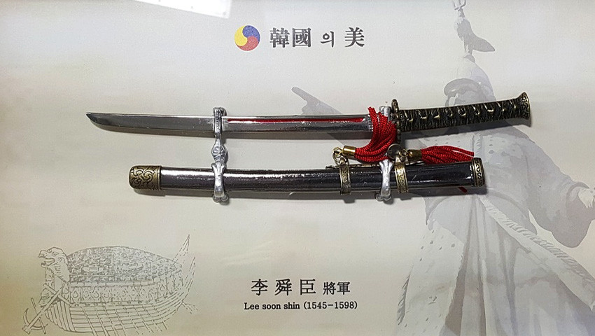 [텍스트: 韓國의美 / 李舜臣 將軍 Lee soon shin (1545-1598)] 금속 장검과 칼집, 붉은 술 장식, 전통 문양 손잡이와 거북선·장수 실루엣 배경이 조화된 벽걸이 장식 액자형 구성