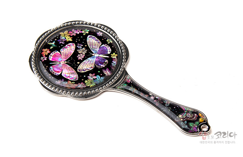 [텍스트: 샵오브코리아 대한민국의 품격까지 전합니다.] 흑색 바탕 위 자개 상감 기법으로 표현된 형형색색 나비와 꽃 문양, 금속 테두리와 손잡이가 조화를 이룬 손거울 디자인