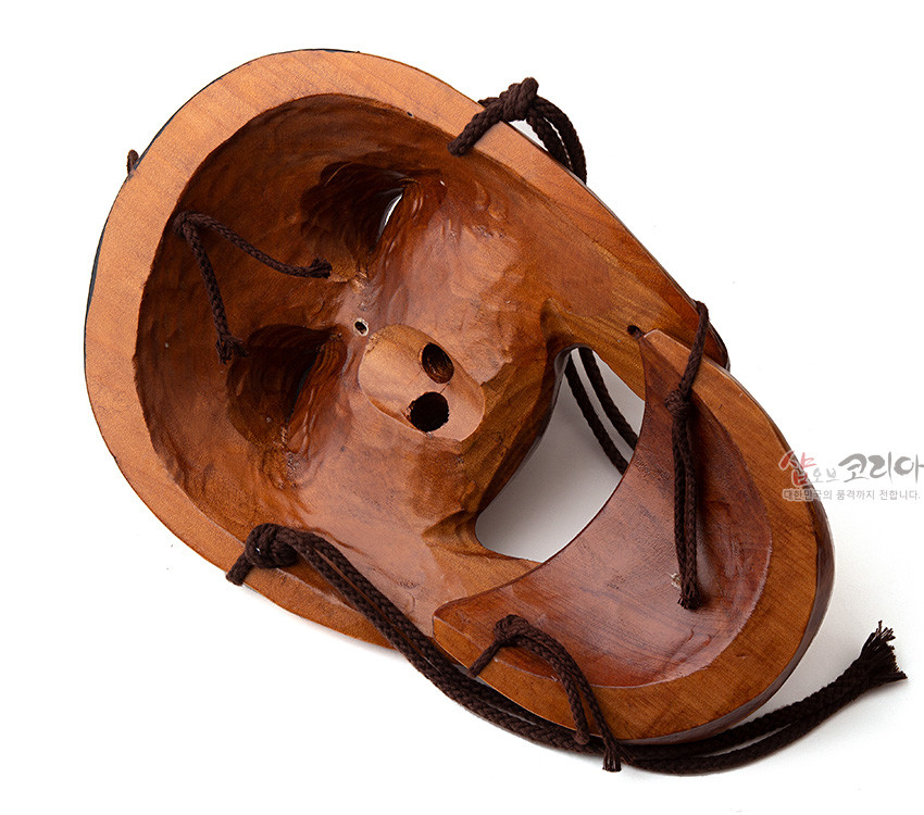 [텍스트: 샵오브코리아 대한민국의 품격까지 전합니다.] 광택 있는 원목을 손조각한 하회탈 안쪽 면과 입체적으로 파인 음영, 짙은 갈색 매듭 끈 장식 모습