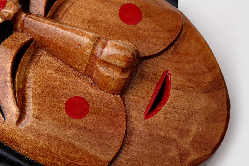 광택 있는 원목을 입체적으로 조각한 전통 부네탈 클로즈업, 붉은 볼 점과 입술 포인트, 자연스러운 나뭇결과 음영 대비가 돋보이는 목가면 디테일 표현