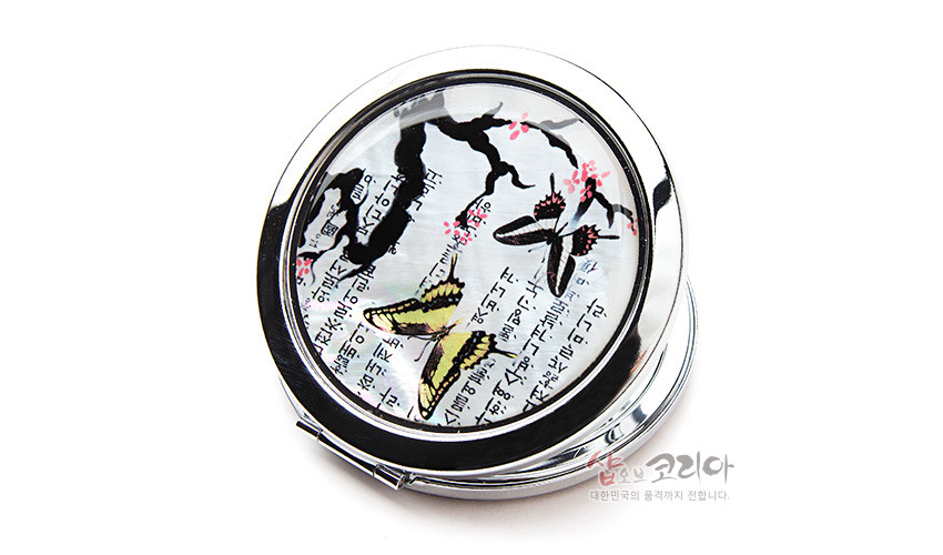 [텍스트: 대한민국의 품격까지 전합니다.] 금속 테두리 안 자개 바탕 위에 매화 가지와 나비, 세로 한글 서체가 어우러진 원형 손거울 디자인