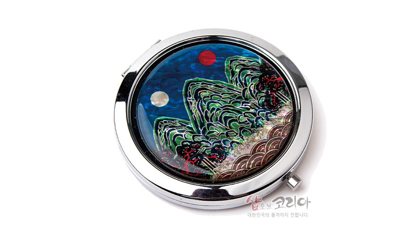 [텍스트: 샵오브코리아 대한민국의 품격까지 전합니다.] 금속 테두리에 자개 상감 기법으로 일월오봉도 산수문을 표현한 원형 손거울, 청록과 남색 대비와 오색 자개의 영롱한 광택이 돋보이는 디자인