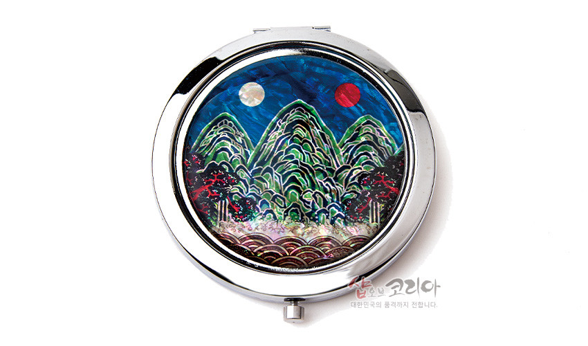 [텍스트: 샵오브코리아 대한민국의 품격까지 전합니다.] 금속 테두리 안에 천연 자개 상감 기법으로 일월오봉도 산수문을 담은 원형 손거울, 남색 하늘과 녹색 산, 붉은 일월의 대비가 돋보이는 구성