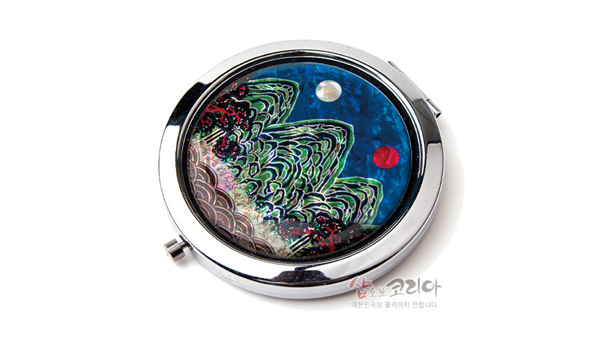 [텍스트: 샵오브코리아 대한민국의 품격까지 전합니다.] 금속 원형 테두리에 청록색 자개 상감 기법으로 표현된 일월오봉도 산수문과 흰 달, 붉은 해가 어우러진 손거울 디자인