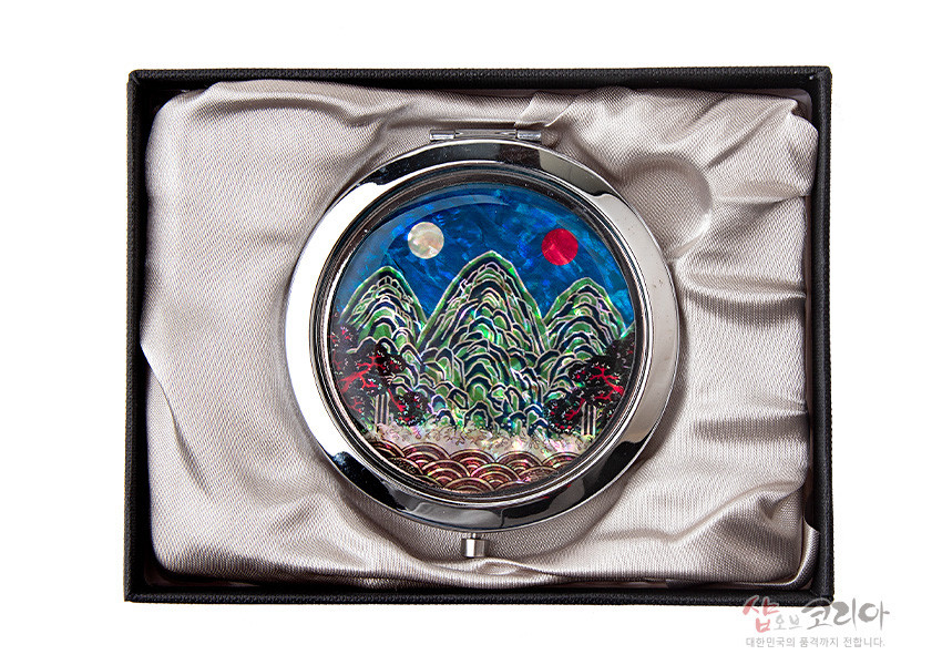 [텍스트: 샵오브코리아 대한민국의 품격까지 전달합니다.] 금속 테두리에 천연 자개 상감 기법으로 일월오봉도 산수문을 표현한 원형 손거울, 청록색 산과 붉은·백색 해와 달의 대비가 돋보이는 디자인